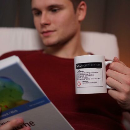 Man reading from a book while holding a caffeine molecule cup with a chemical label
