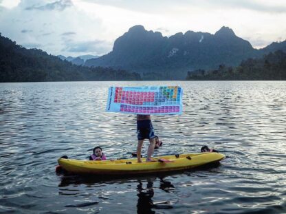 Periodic table towel presented by man standing in a kayak in a lake