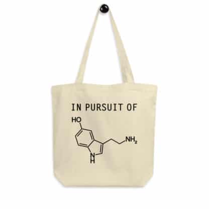 A tote bag with a print that says "In Pursuit of" followed by a serotonin molecule